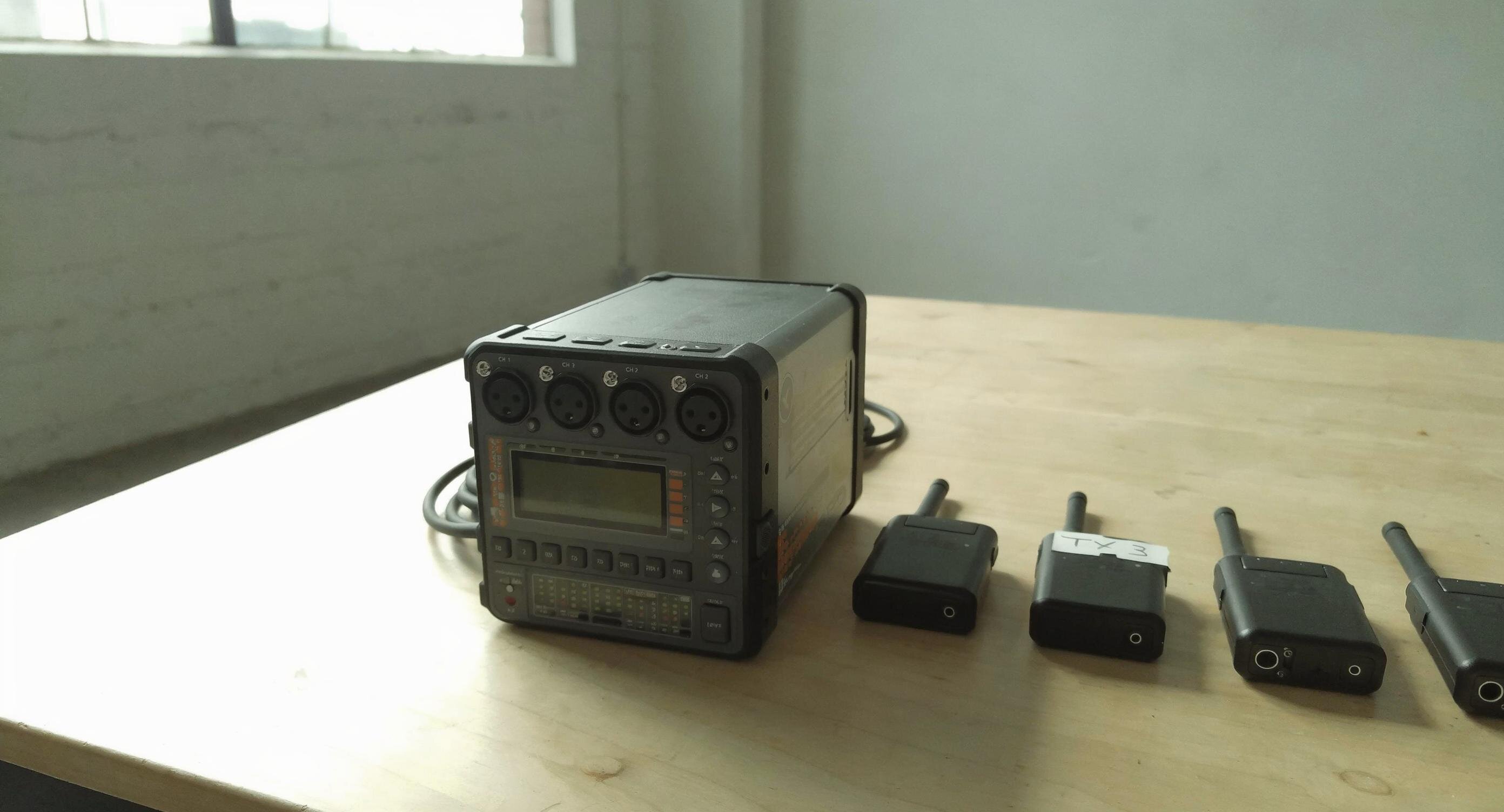 Professioneller Field-Audiomischer mit XLR-Eingängen neben mehreren Drahtlos-Funkstrecken auf einem Holztisch